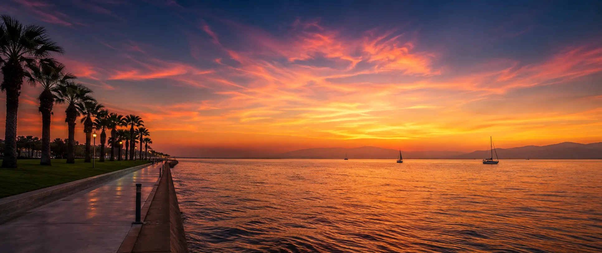 Le front de mer d’İzmir au coucher du soleil, palmiers en silhouette et voiliers sur le golfe